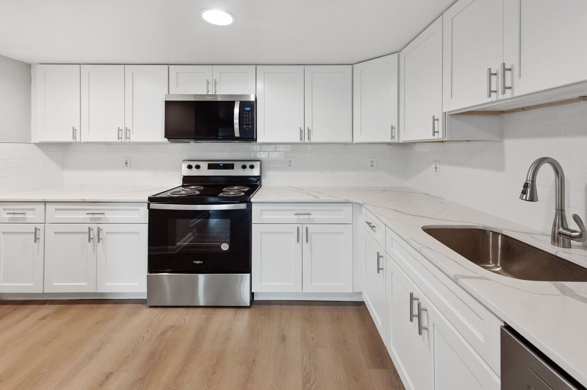 White kitchen with stainless steel stove, microwave, sink, and white cabinets.