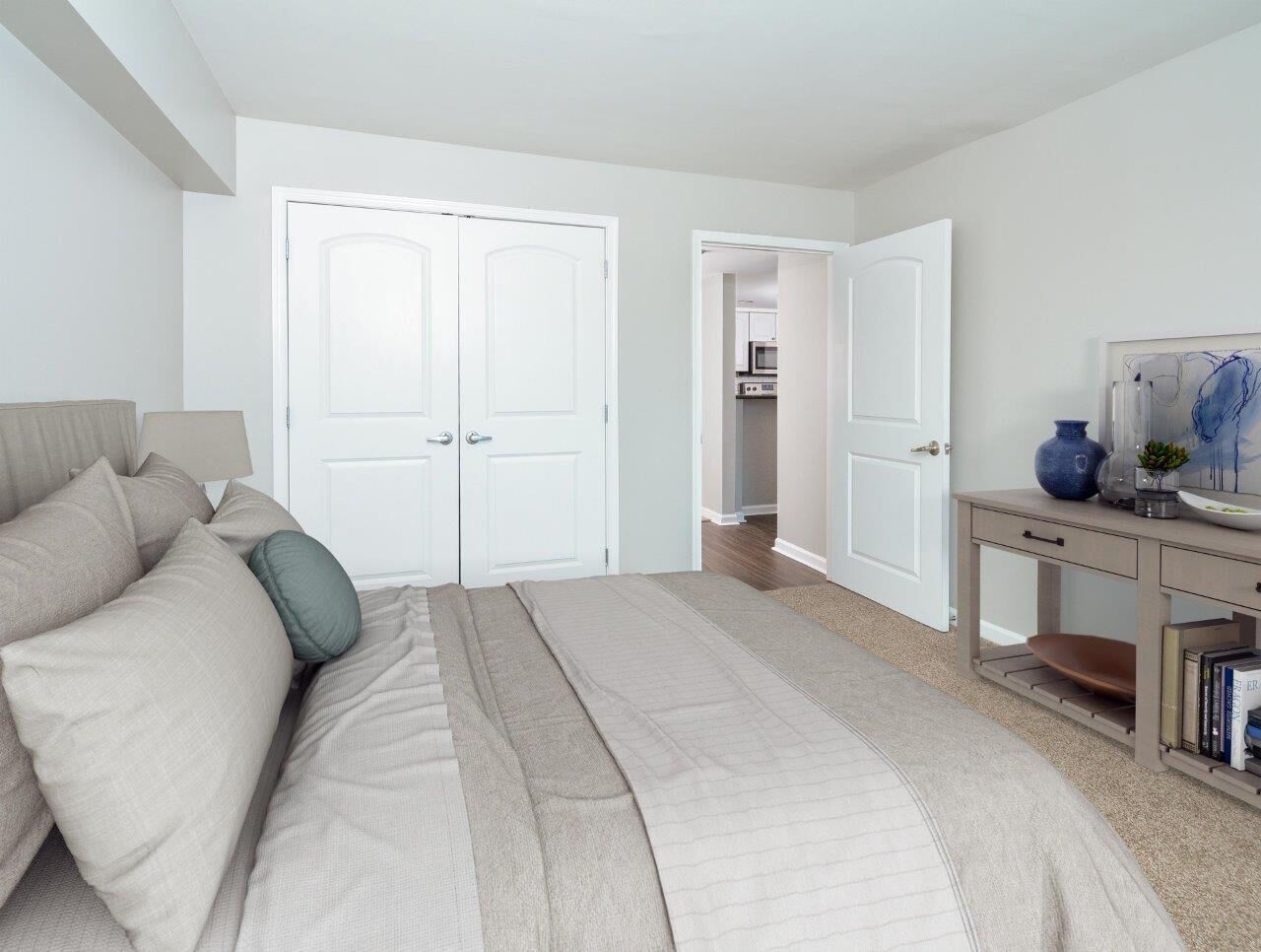Bedroom with a neatly made bed, beige bedding, dresser with decor, and an open doorway to a hallway.