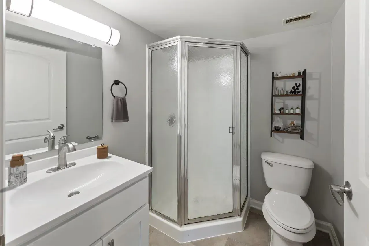 Bathroom interior in a modern apartment with a white vanity, frosted glass shower, and toilet.