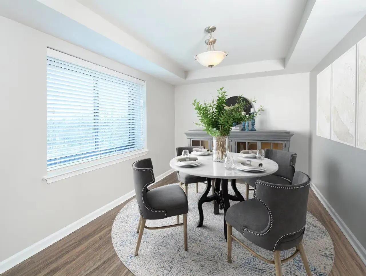 Round marble dining table with four gray upholstered chairs in a bright dining nook by a window.