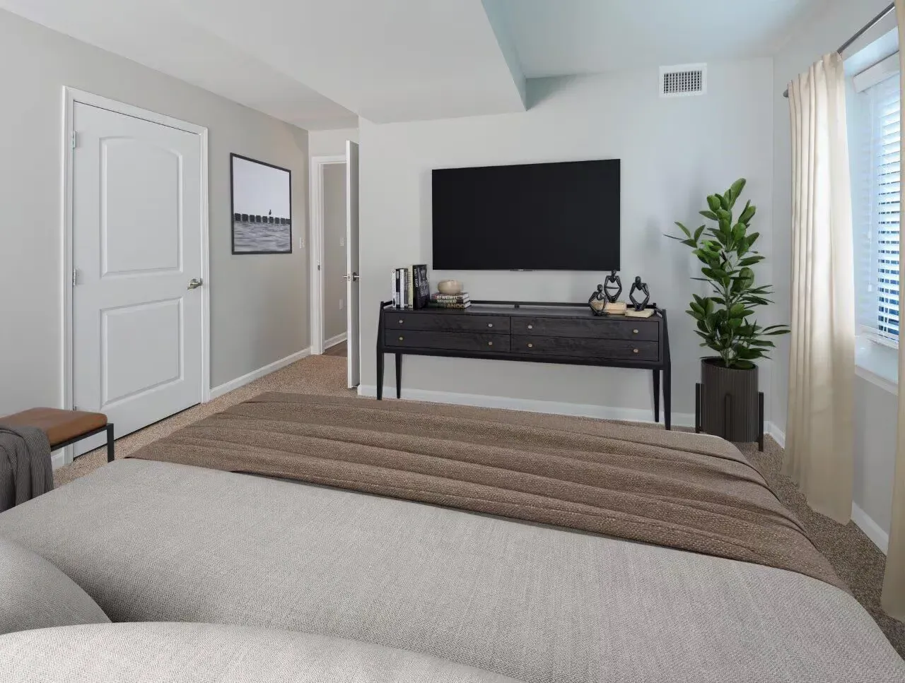 Bedroom featuring a bed, a dark console with a mounted TV, a tall plant, and a window with cream curtains.
