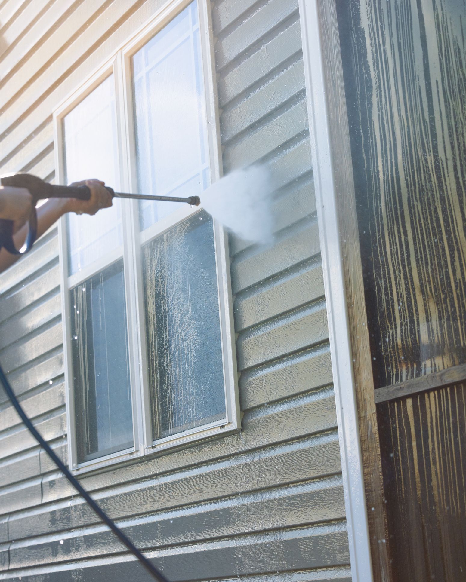 A man is cleaning a vinyl siding with pressure washing.