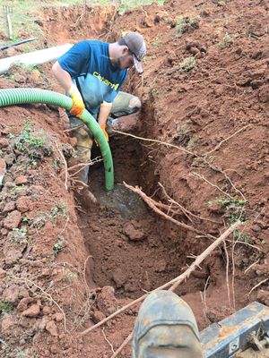 Person using a hose to remove water from a trench. Brown soil, green hose.
