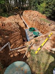 Construction site: a septic tank installation in a yard. Trenches, pipes, and dirt surround the tank.