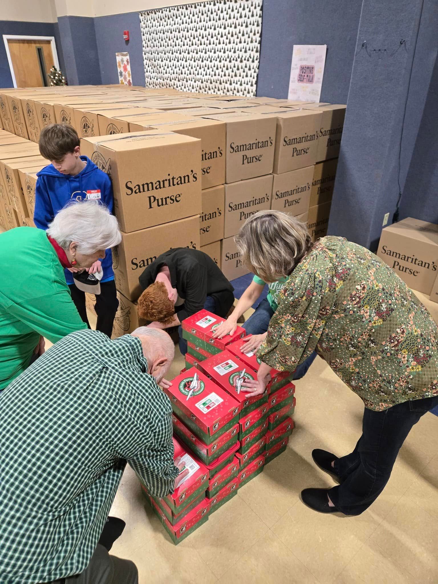 People stacking red boxes, possibly for charity, in a large room near stacks of brown boxes.