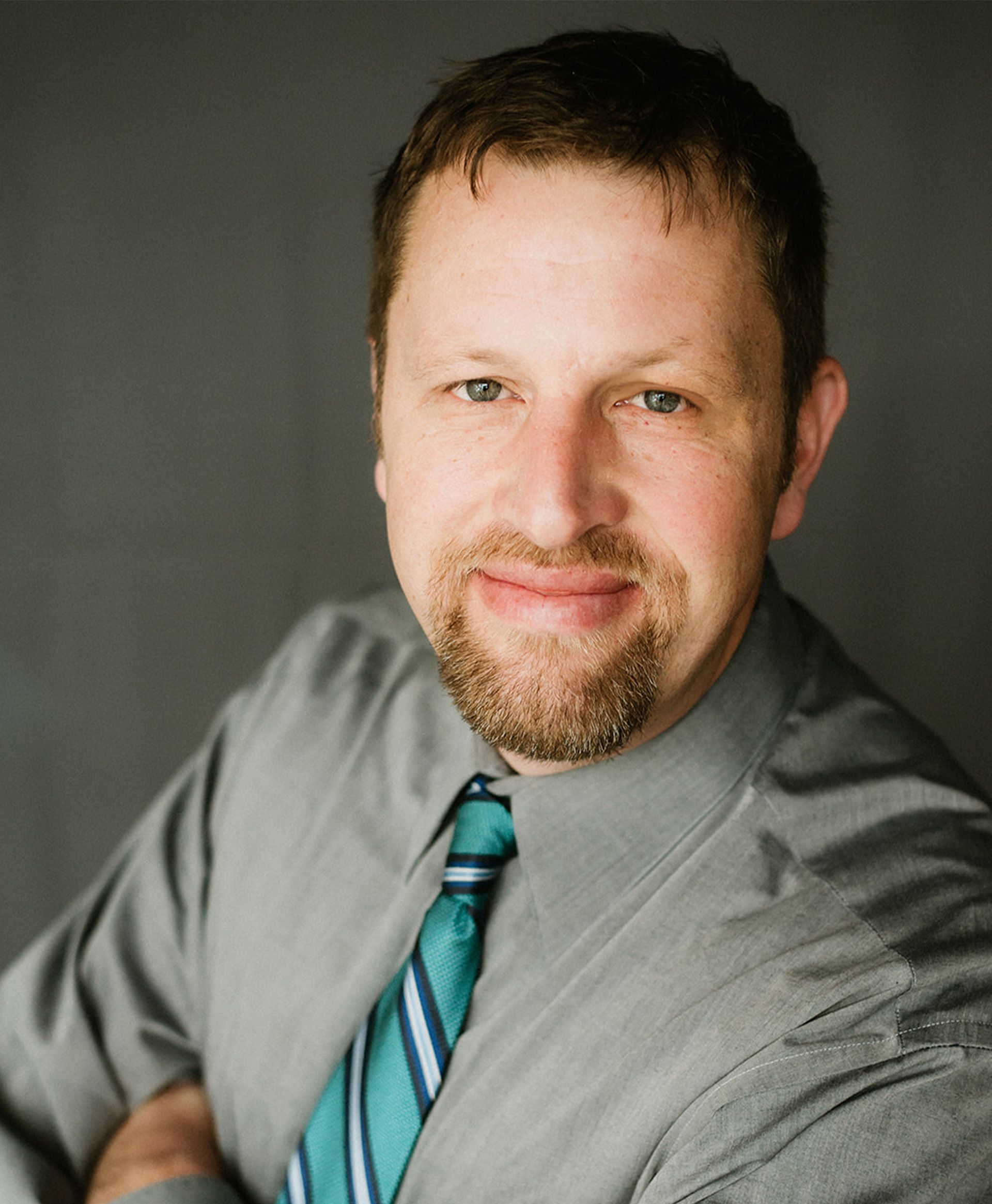 A man with a beard is wearing a gray shirt and a green tie.