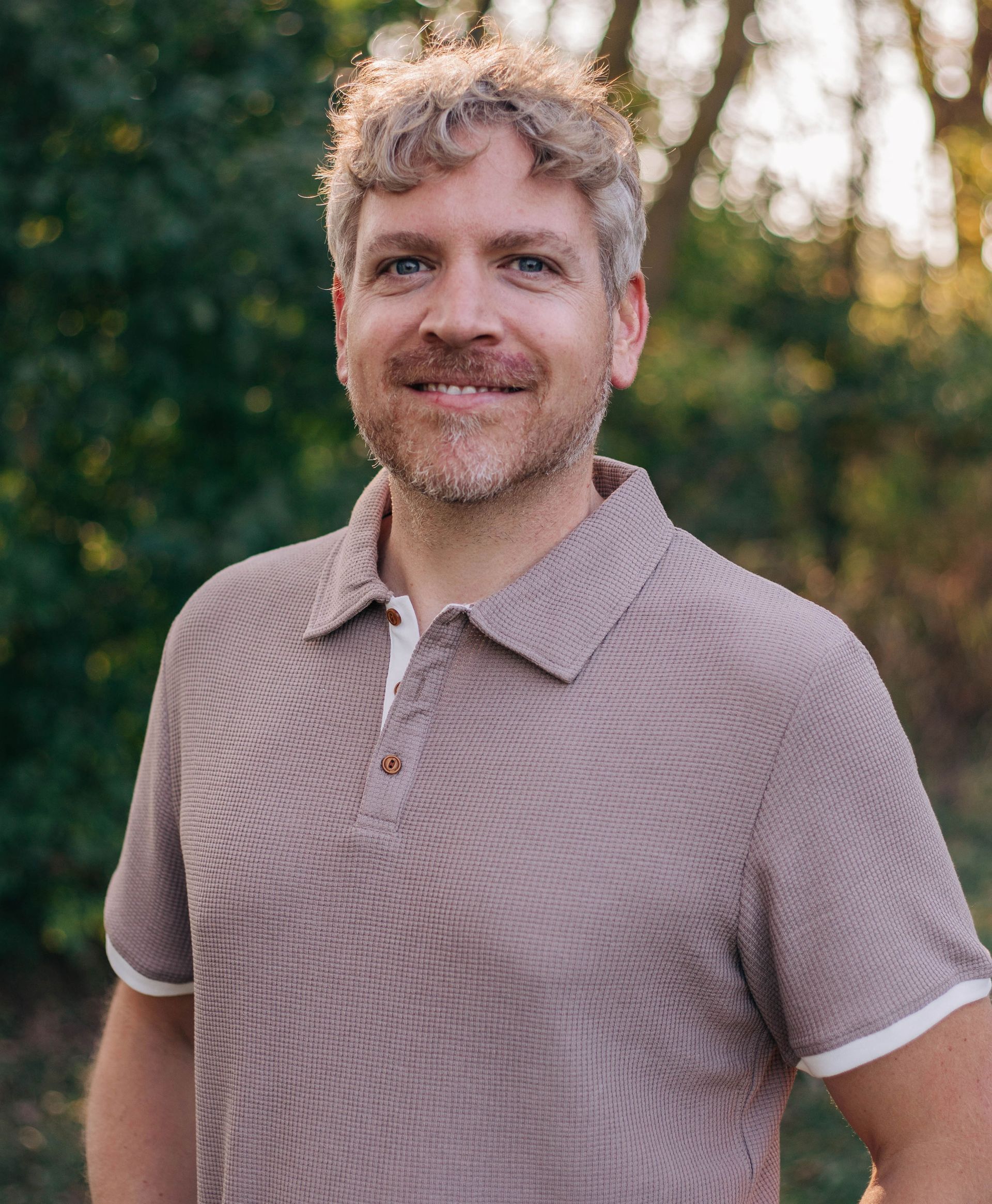 A man with a beard is wearing a polo shirt and smiling for the camera.