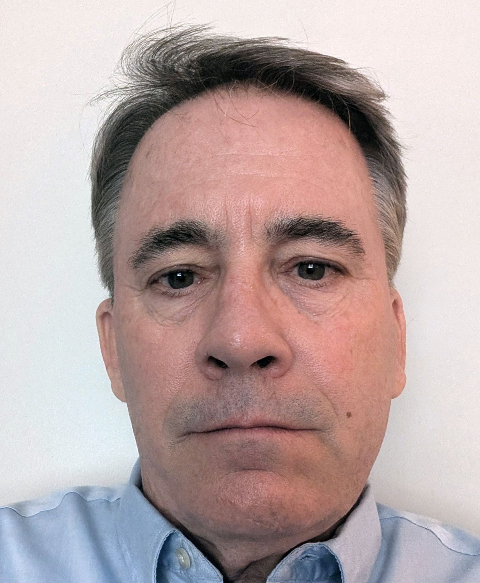 A man in a blue shirt is looking at the camera with a serious look on his face.