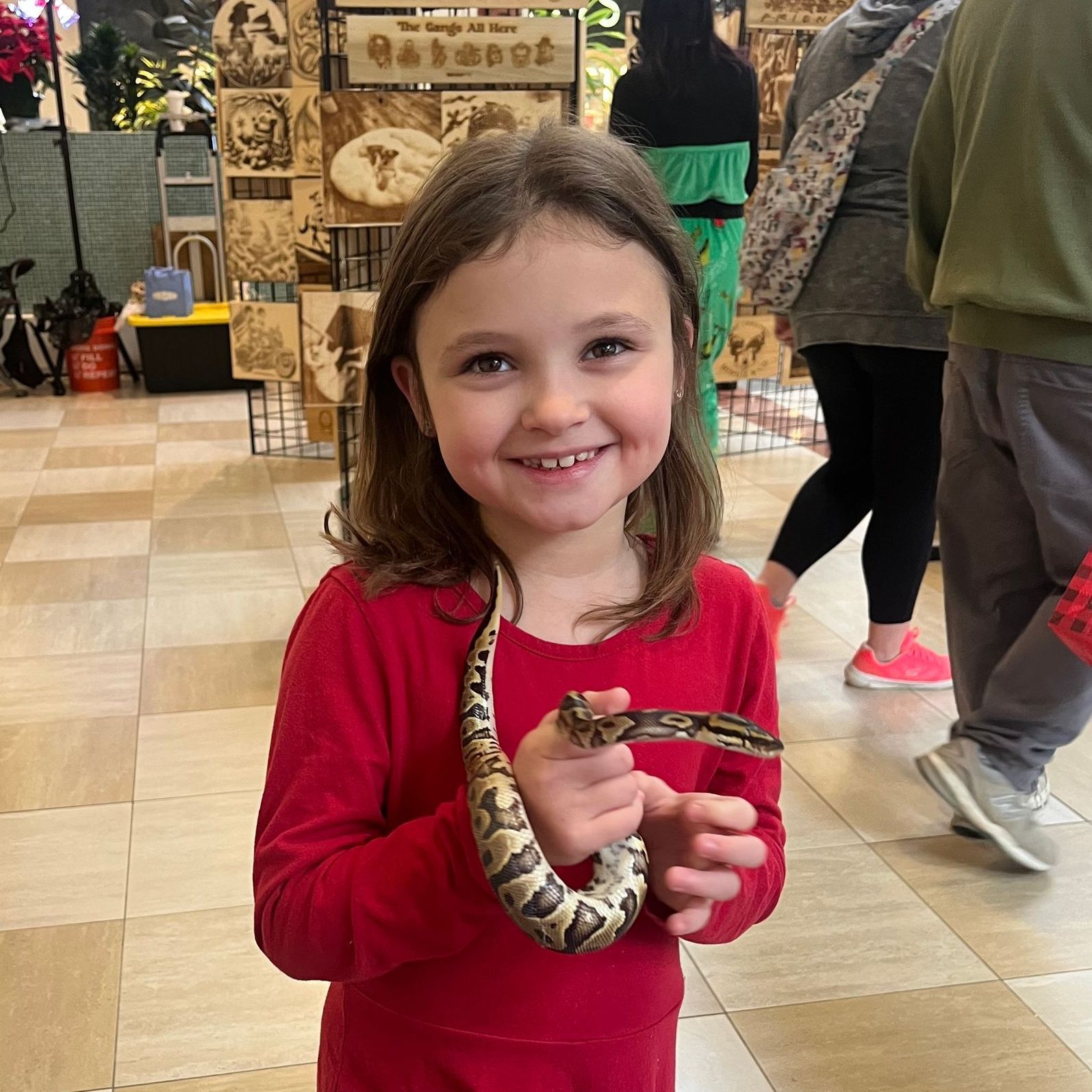 A little girl in a red shirt is holding a snake around her neck