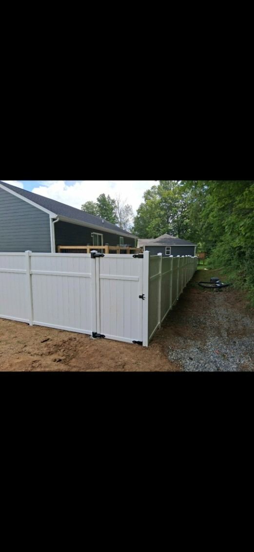 White vinyl fence with gates along a house and gravel driveway.