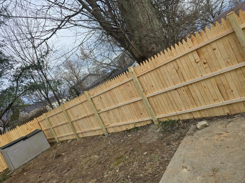 Wooden picket fence in a yard, trees in background, overcast sky.