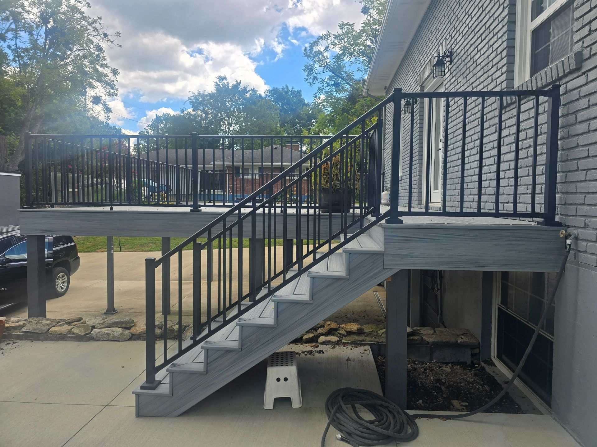 Deck and stairs with black railing, gray steps, attached to a brick building.