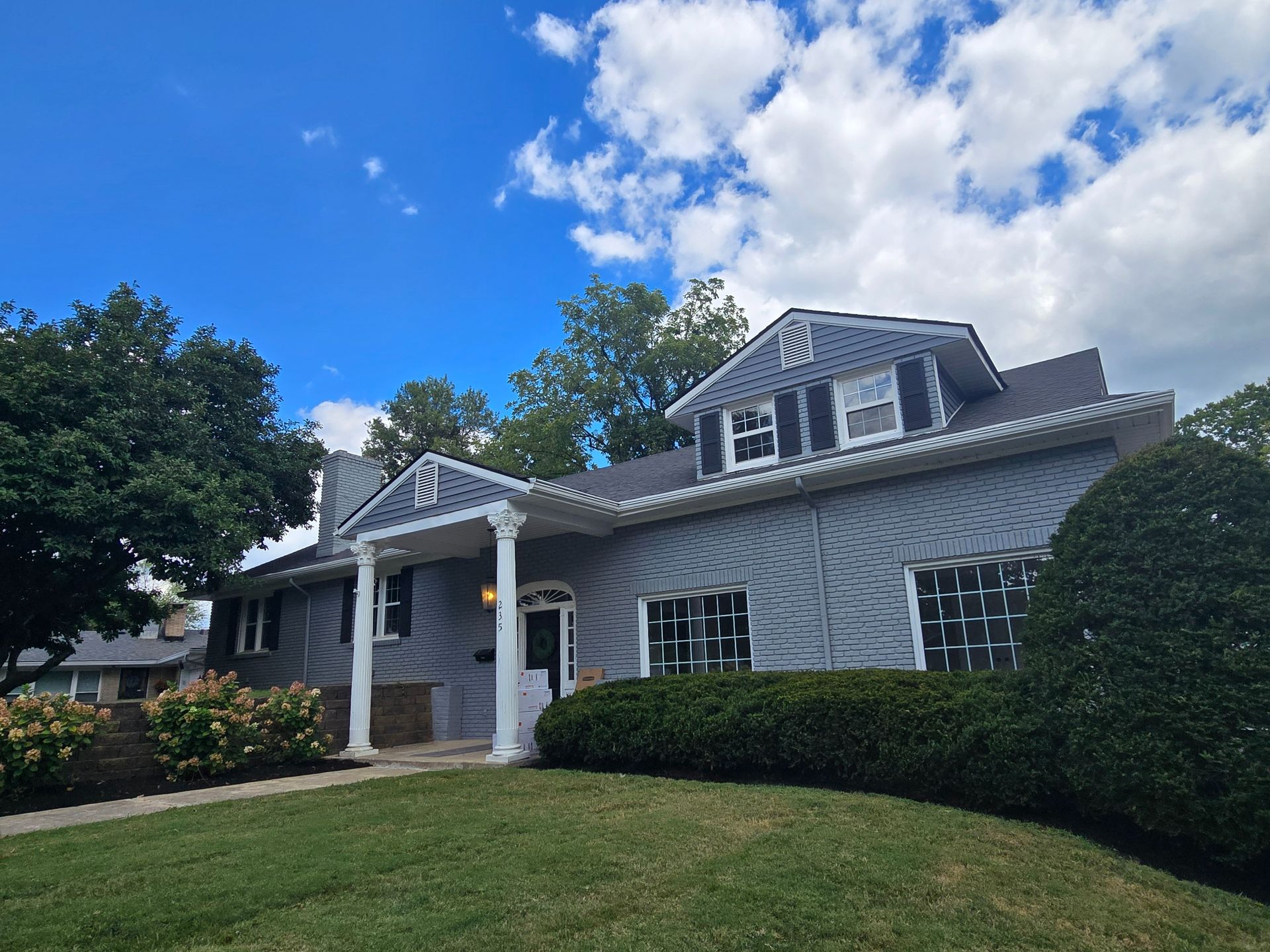 Blue house with white trim, porch with columns, under a blue sky with clouds.