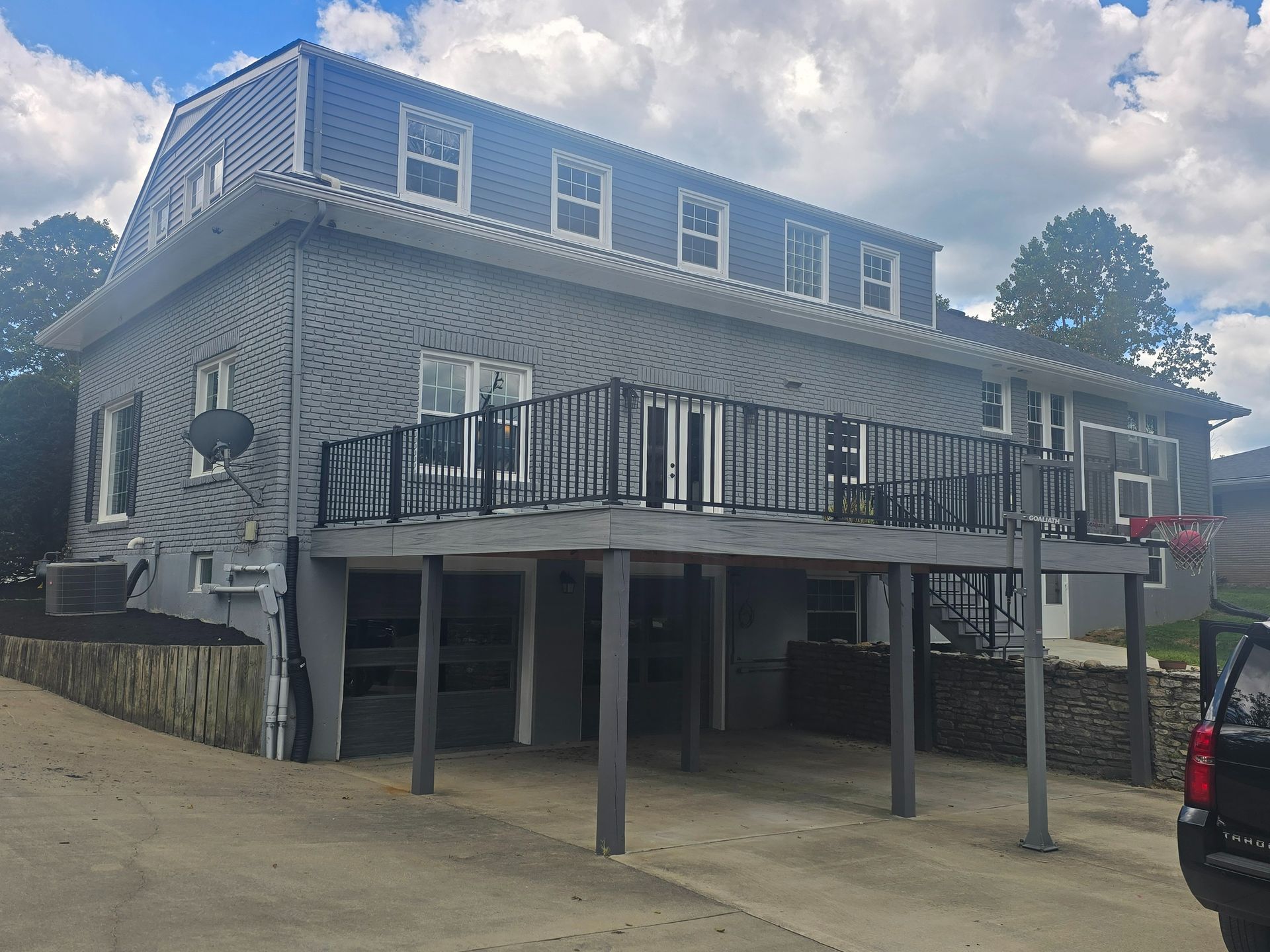 Two-story gray house with a deck, multiple windows, and a driveway on a cloudy day.