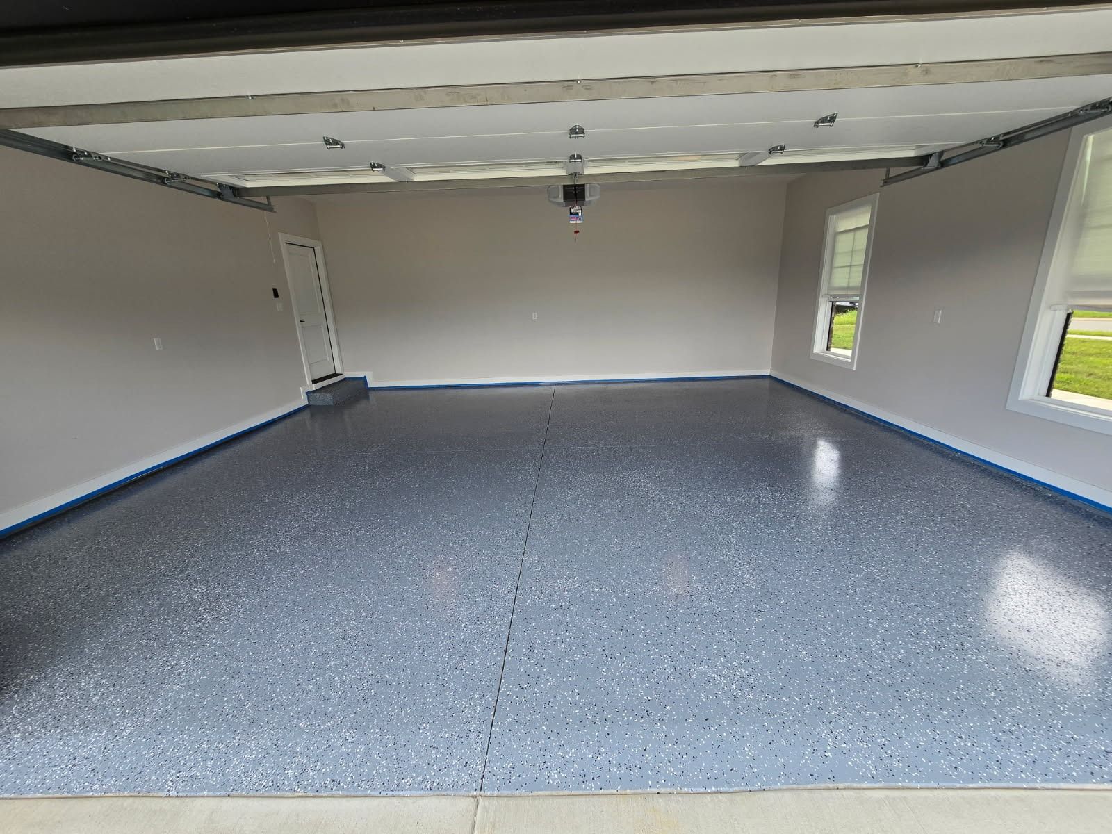 Empty garage with a gray speckled epoxy floor, beige walls, and white trim.