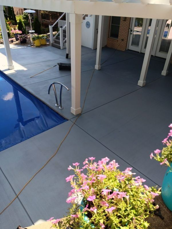Poolside patio with gray concrete, white pergola, and blue pool. Pink flowers in foreground.