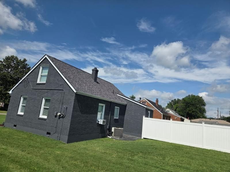 Dark gray house with white trim, a dark roof, and a white fence against a blue sky with clouds.