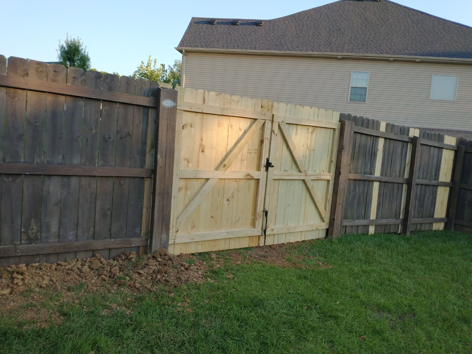 Wooden gate in a backyard fence, built between weathered wooden fence sections, with a house in the background.