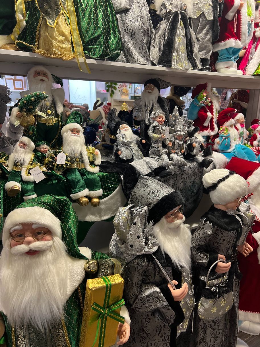 Santa Claus figurines displayed in a store, showcasing various styles with green, silver, and red outfits.