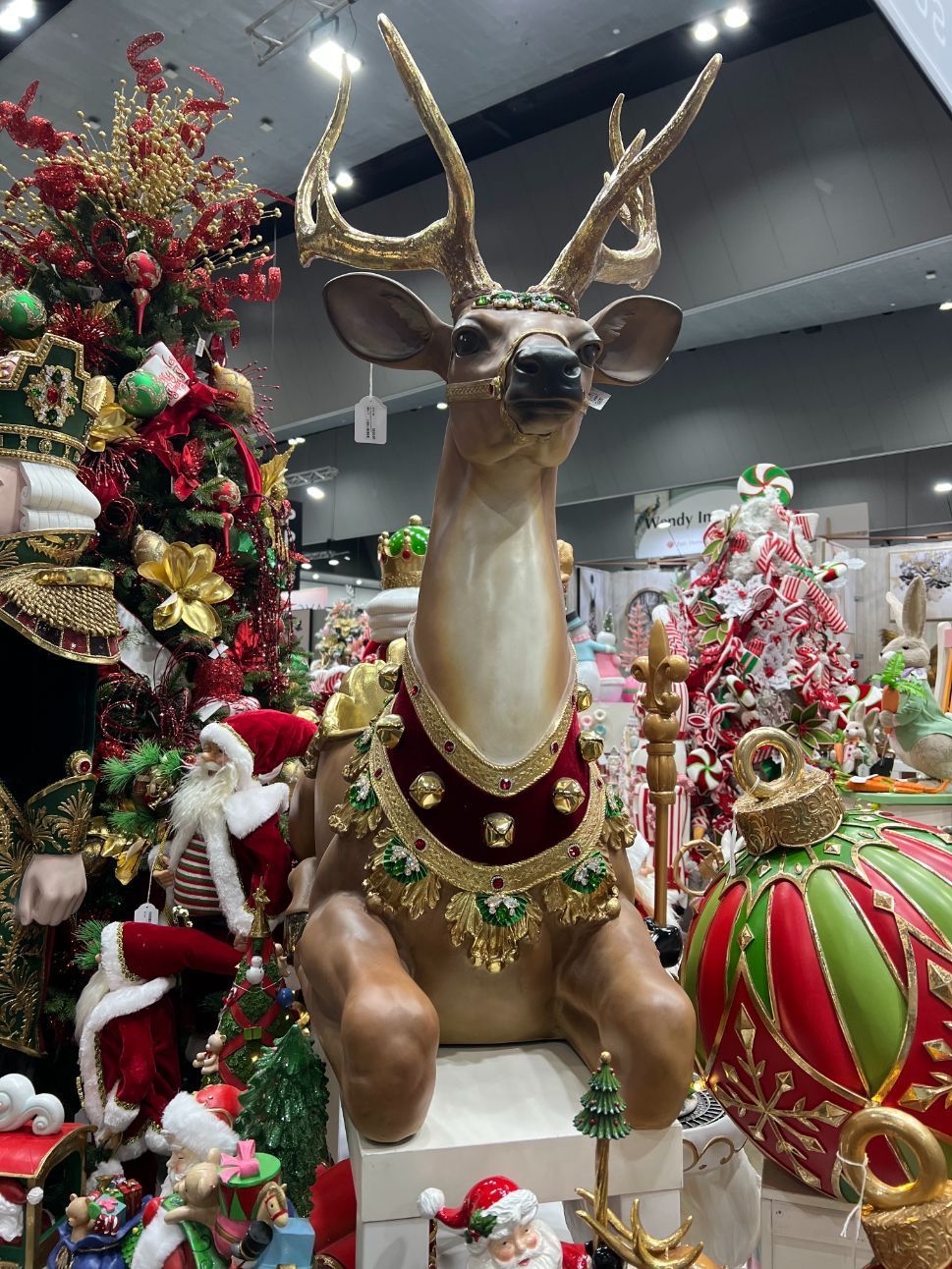 Large reindeer statue with gold antlers, adorned in festive decorations at a Christmas market.