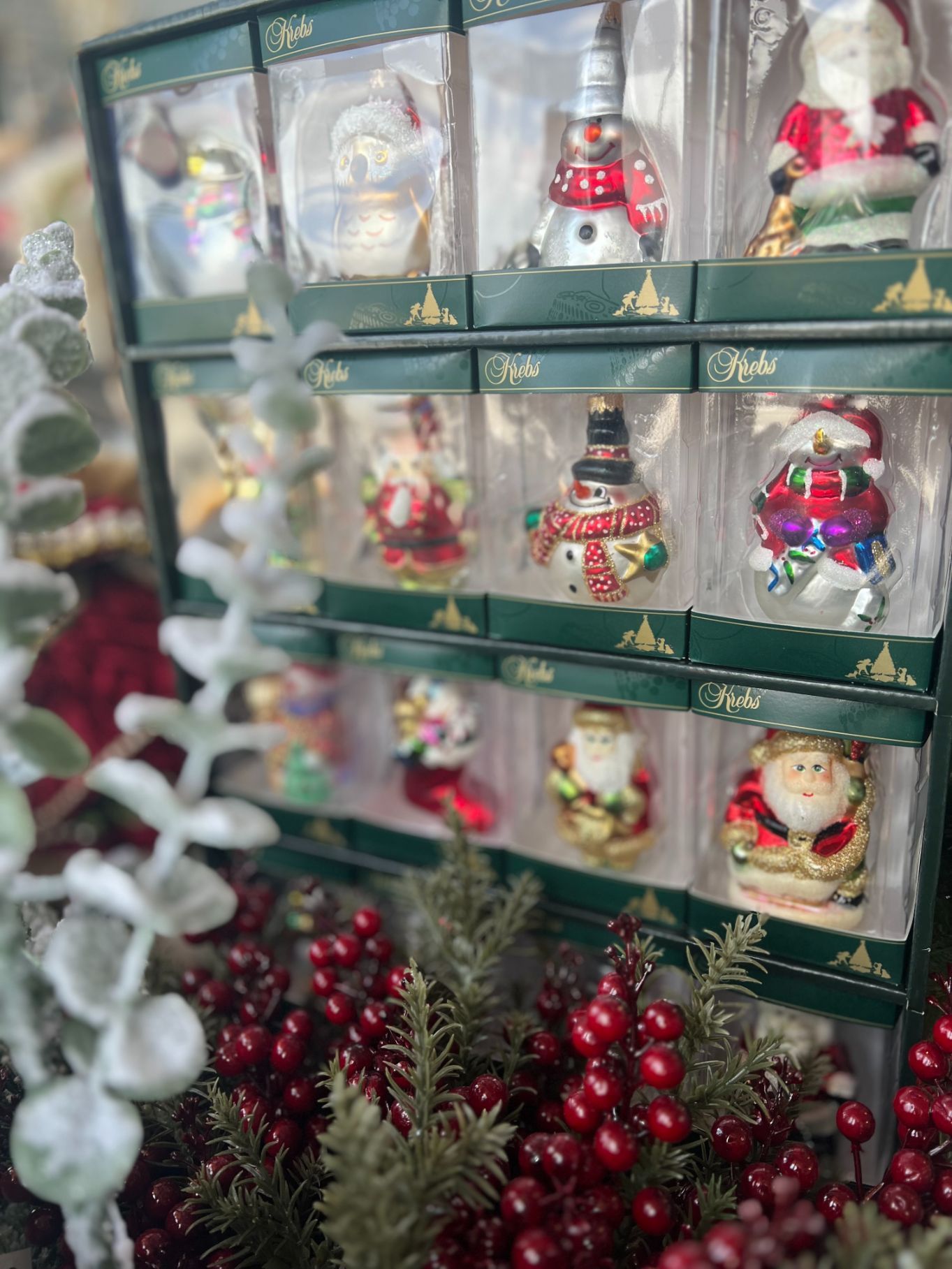 Christmas ornaments in boxes, arranged on a shelf, with red berries and green foliage in the foreground.