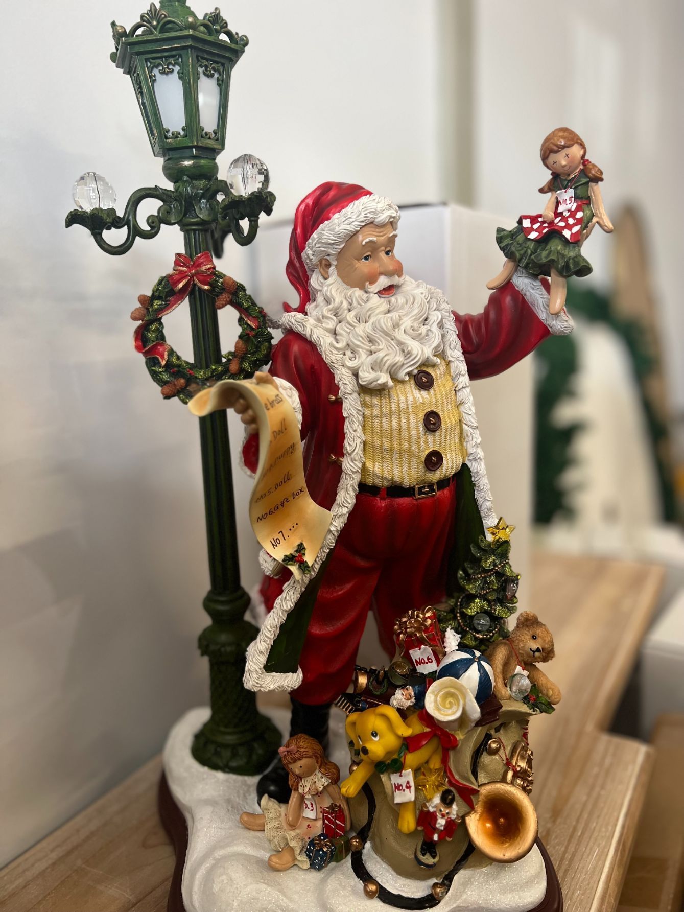 Santa Claus figurine with list, lamp post, toys, and a child.