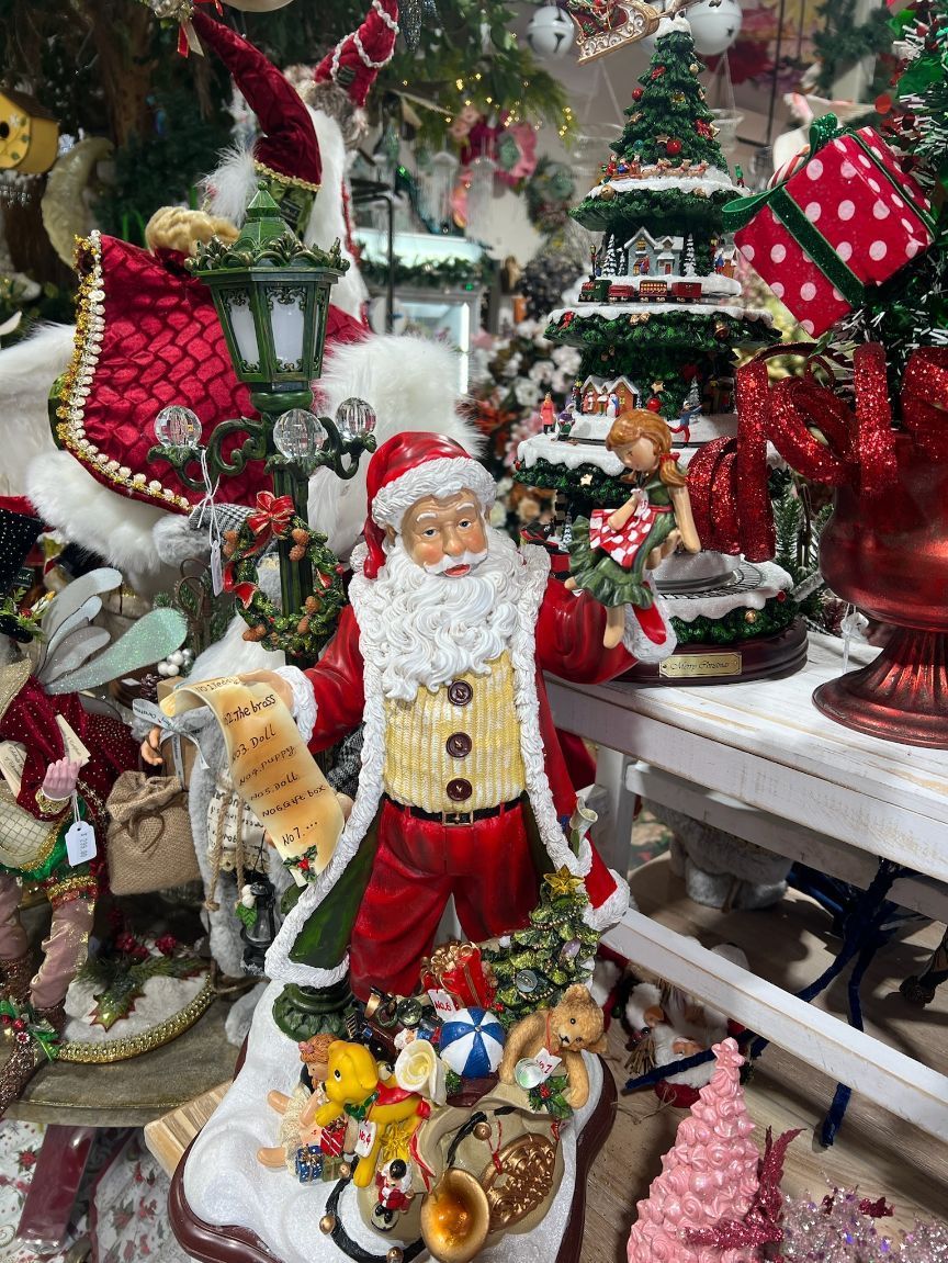 Santa Claus figure surrounded by Christmas decorations. Red suit, holding list, standing.
