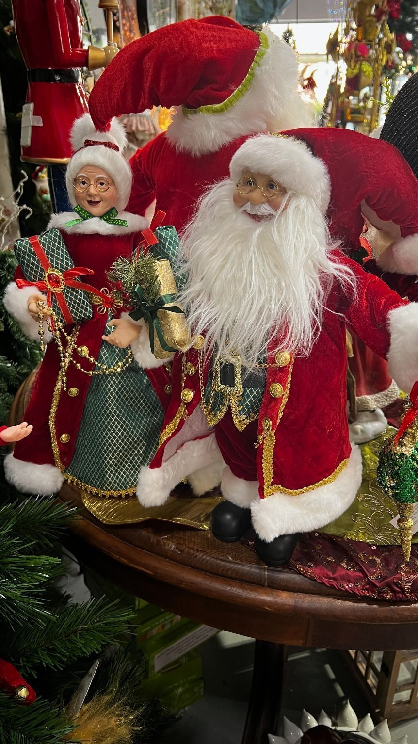 Santa figures on a round table, dressed in red and white. Mrs. Claus and elves surround them.