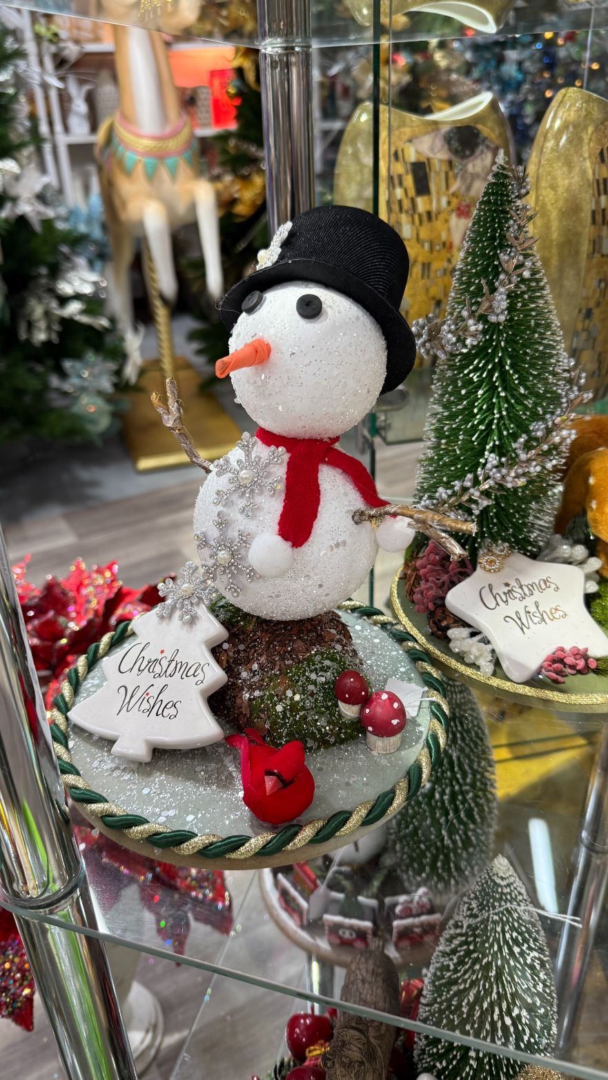 Snowman figurine with black hat, red scarf, and festive decorations on a shelf.