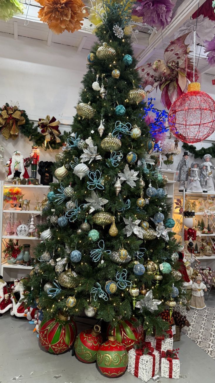 Christmas tree decorated with blue, gold, and silver ornaments in a shop setting with other decorations.