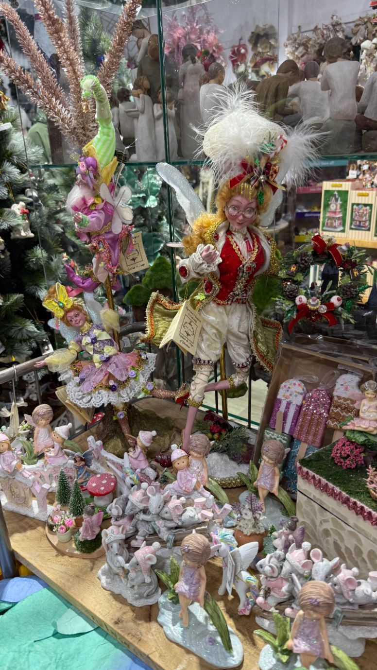 Display of ornate figurines and sculptures in a shop. Colorful, fairy-like designs with floral and feathered details.
