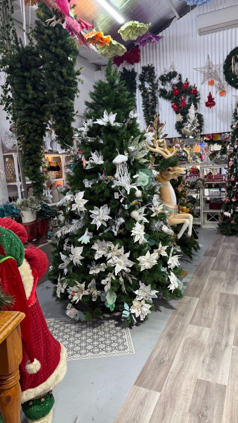 Christmas tree decorated with white flowers in a store with other holiday decorations.