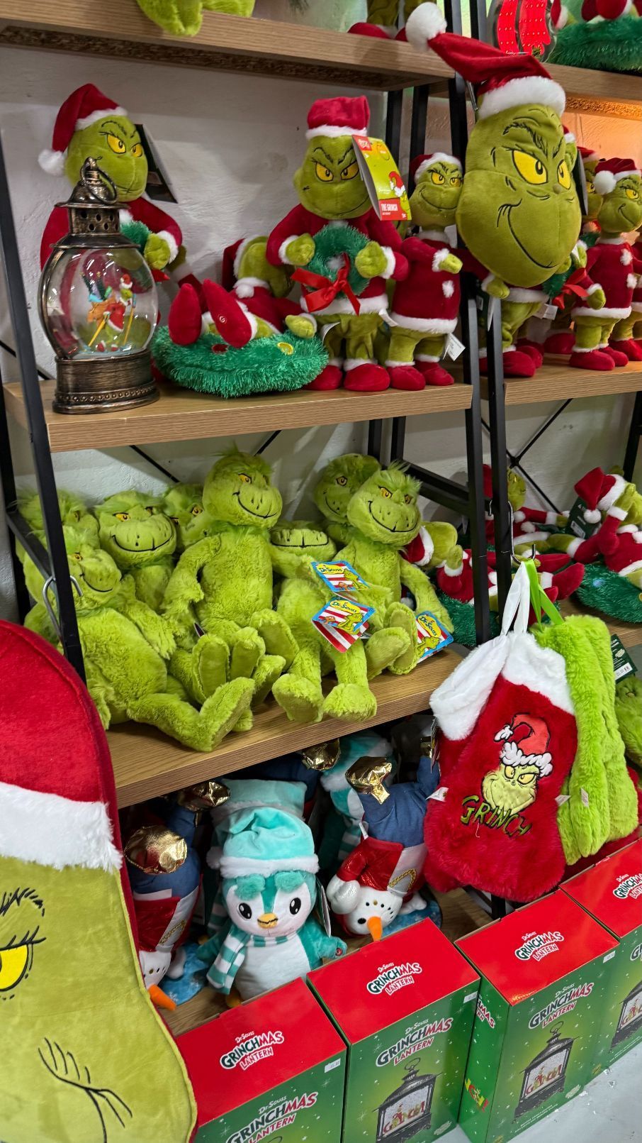 Shelves packed with Grinch plushies and Christmas decorations, various sizes and poses, green and red.