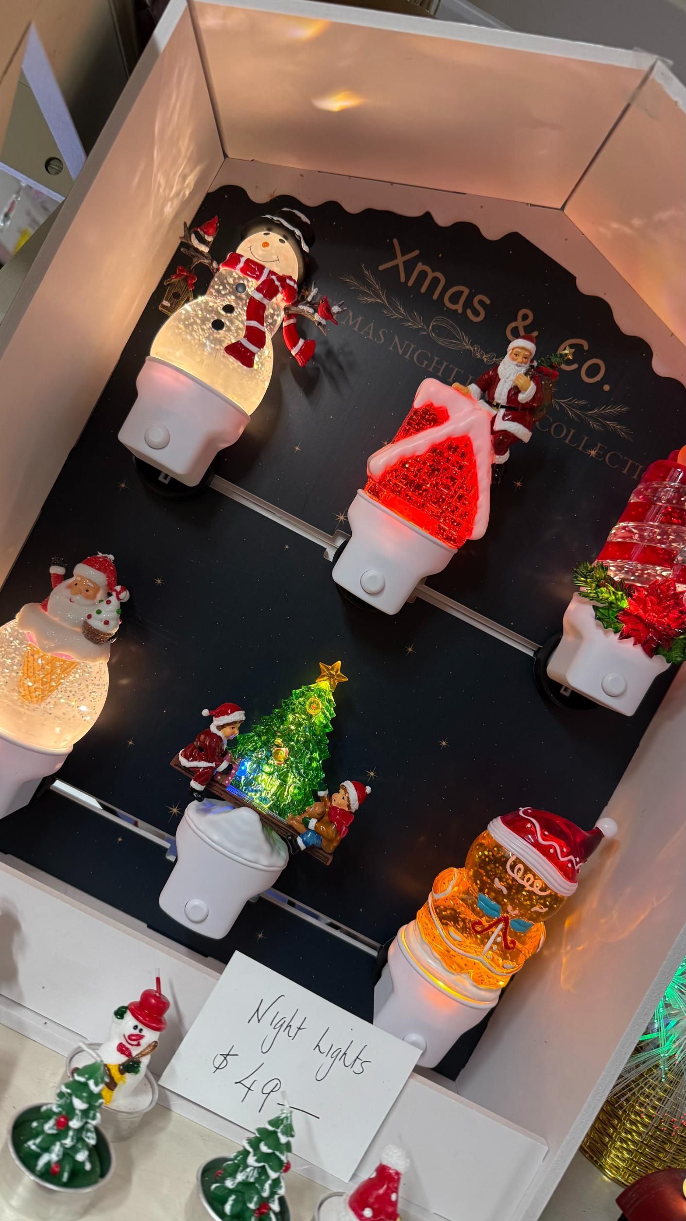 Display of Christmas-themed night lights: snowman, Santa hat, tree, and Santa. White base, colorful decorations, and a black display board. | Jingle Bell Christmas