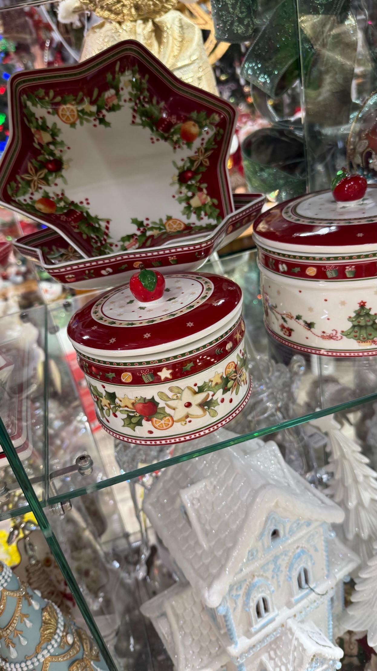 Christmas-themed ceramic serving dishes with red and floral patterns, set in a glass display case. | Jingle Bell Christmas
