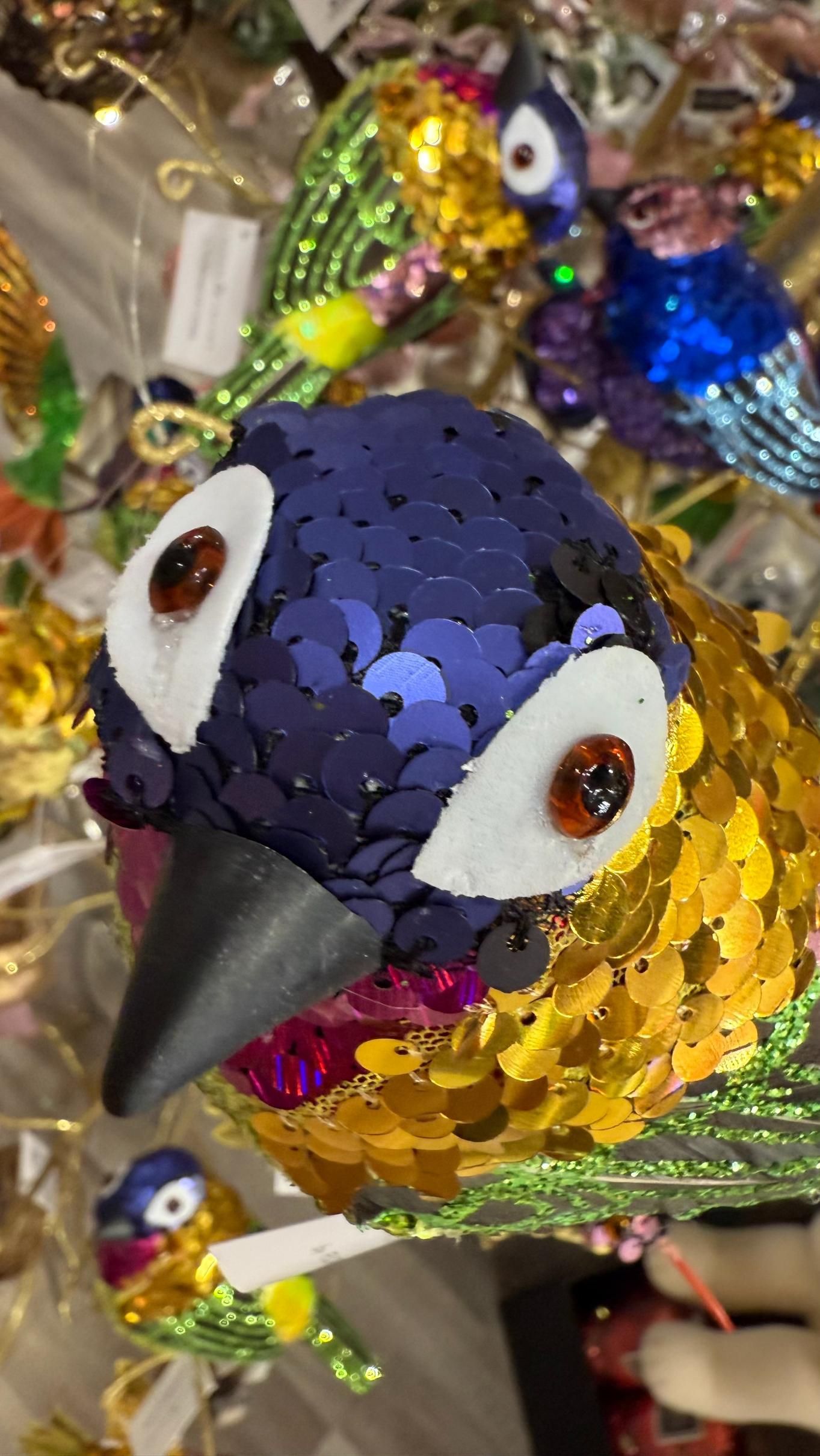 Close-up of a bird ornament with blue, gold, and pink sequins, and a black beak. | Jingle Bell Christmas