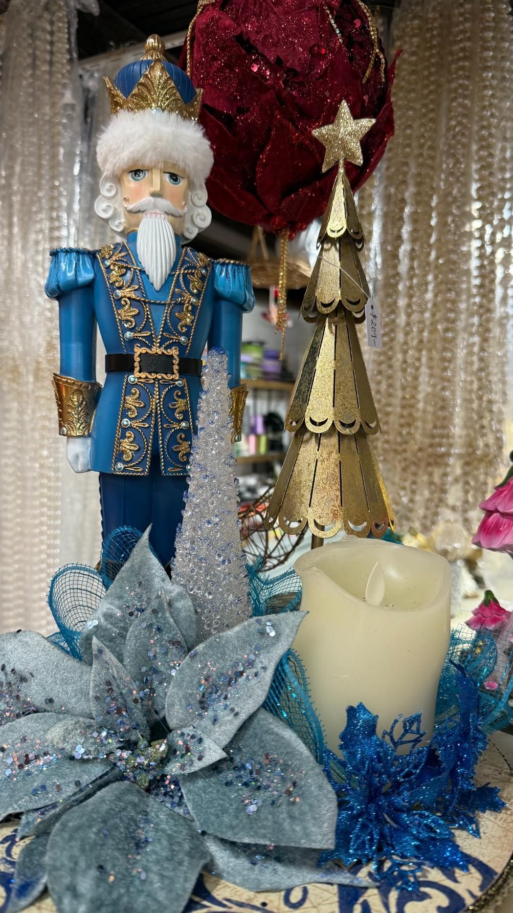 A Christmas display with a blue nutcracker, gold tree, candle, and sparkly flowers. | Jingle Bell Christmas