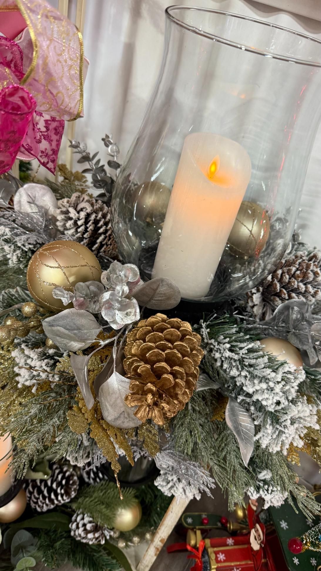 Festive centerpiece with lit candle in a glass jar, gold ornaments, pinecones, and frosted greenery. | Jingle Bell Christmas