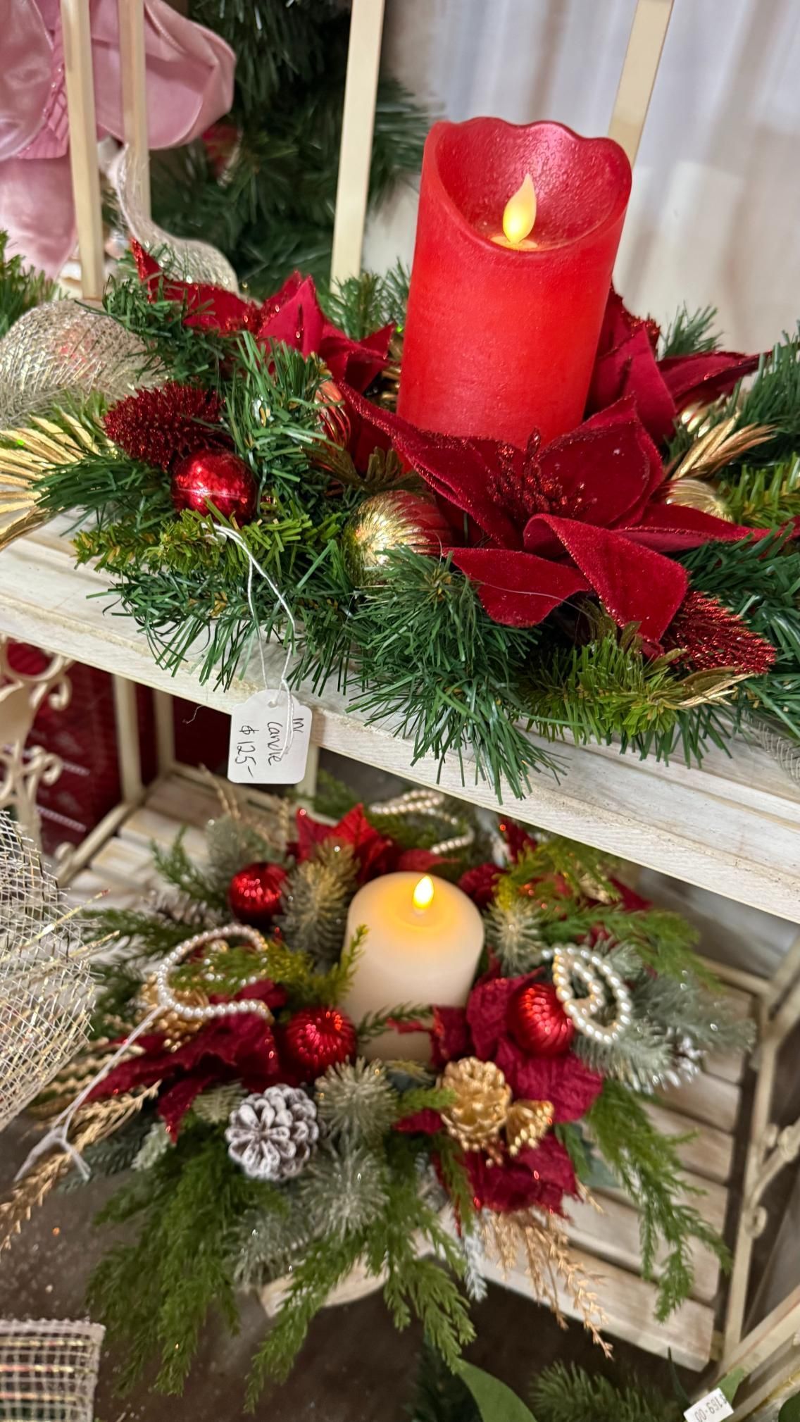 Christmas floral arrangements on a white shelf, featuring candles, red poinsettias, and ornaments. | Jingle Bell Christmas