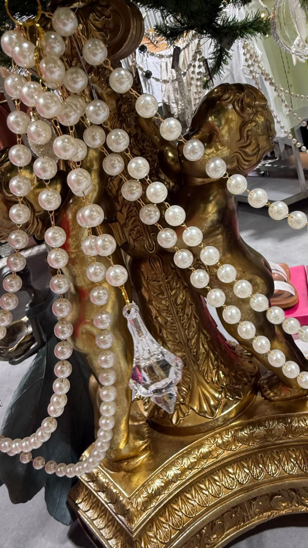 Golden cherub statue draped with pearl beads and a crystal ornament. | Jingle Bell Christmas