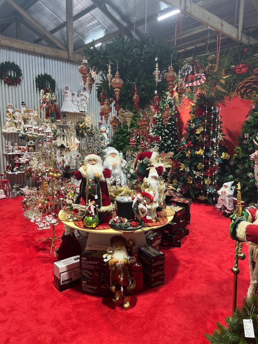A Christmas display in a shop with trees, ornaments, Santas, and red carpet.