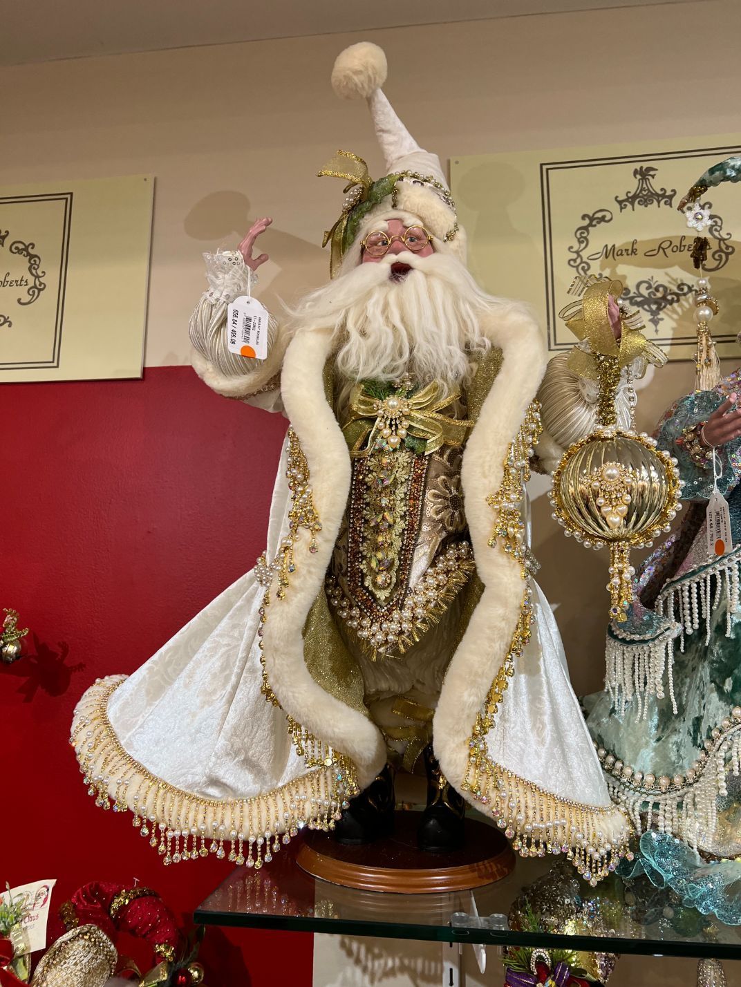 Elegant Santa Claus figurine in white and gold, holding gifts, against a red background.