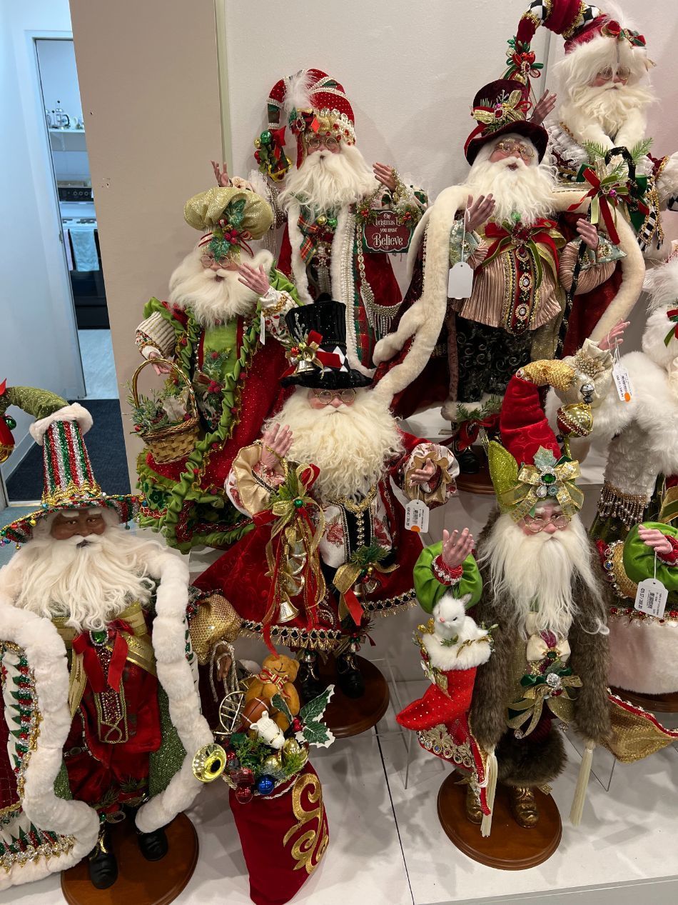 Festive Santas in elaborate red, green, and gold outfits, displayed on a shelf.