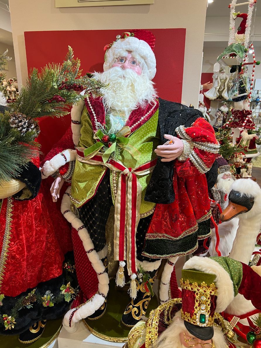 Santa Claus figure in elaborate green, red, and black outfit, surrounded by other Christmas decorations.