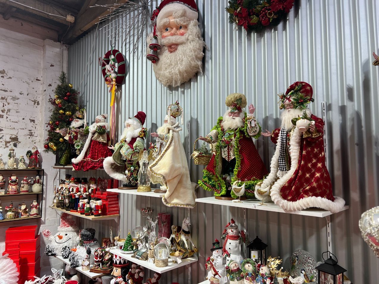 Christmas decorations displayed on shelves against a corrugated metal wall. Santas, snowmen, wreaths, and ornaments.