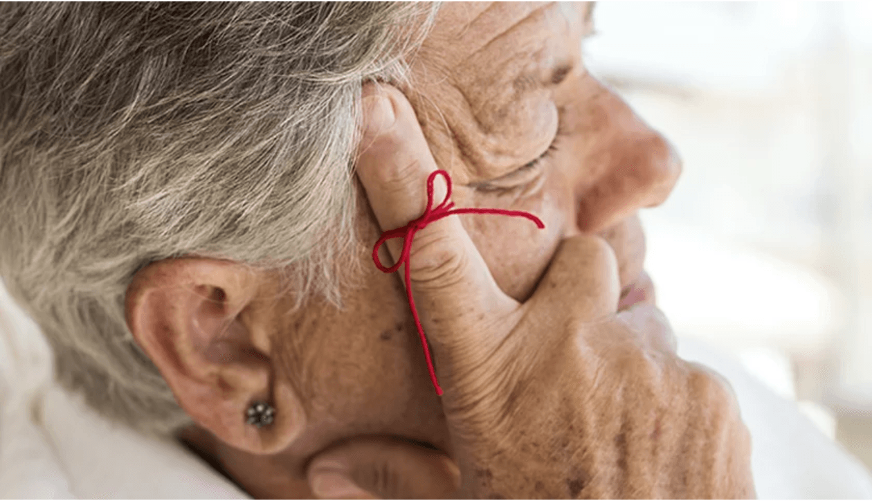 older woman with finger pressed to temple with red string around finger