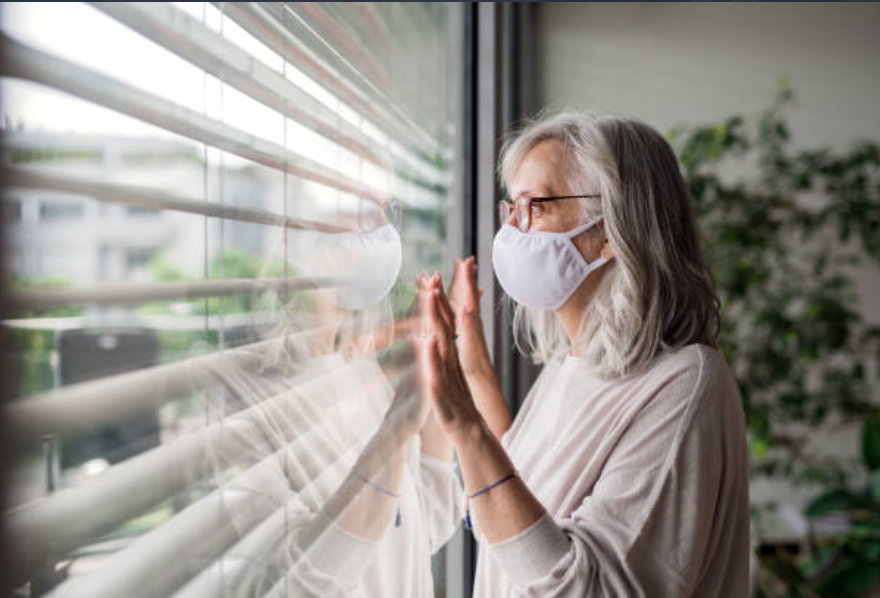 elderly woman wearing mask looking out window