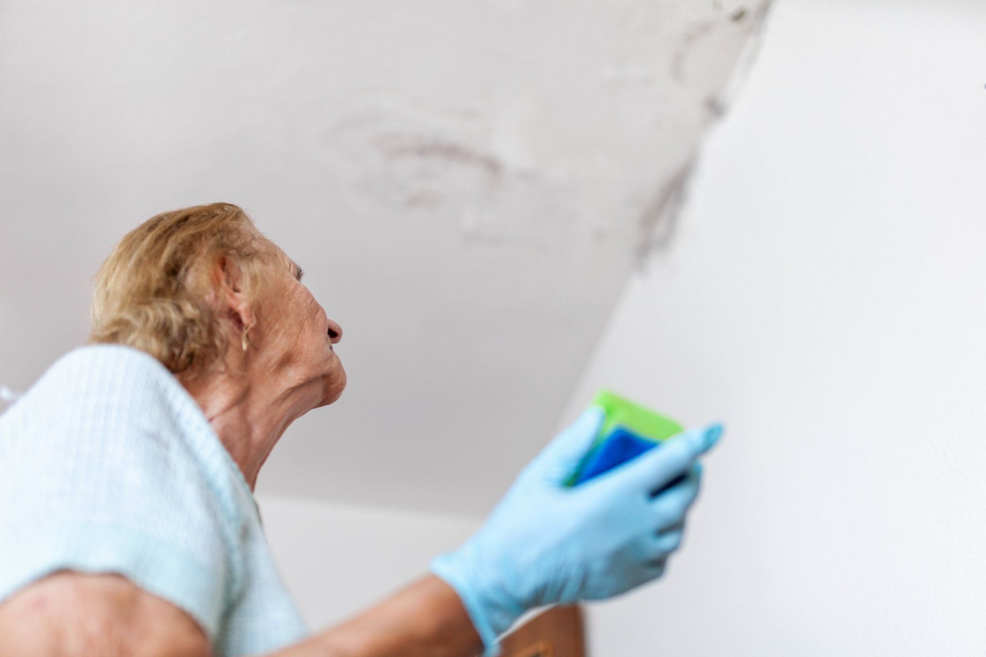 Senior cleaning up water damage mold from a wet wall.