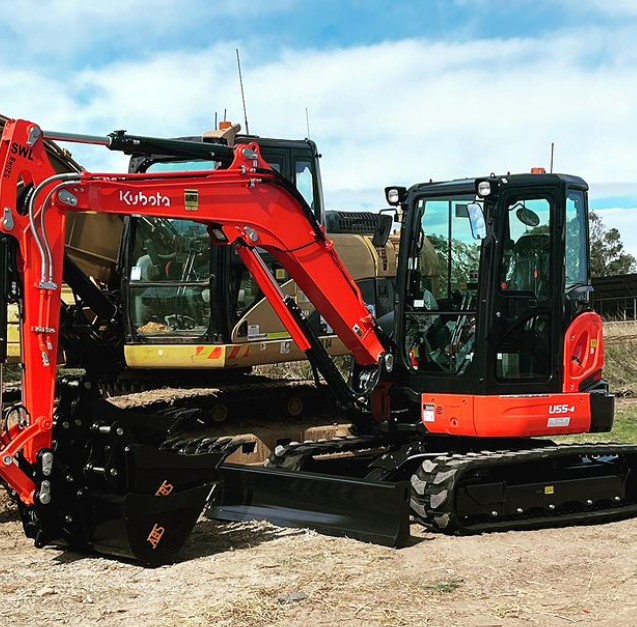 A red excavator is parked next to a black excavator.