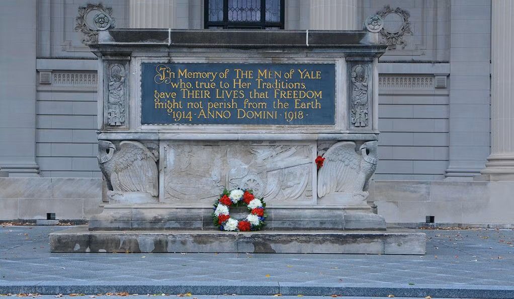 A statue with a wreath of flowers on it in front of a building.